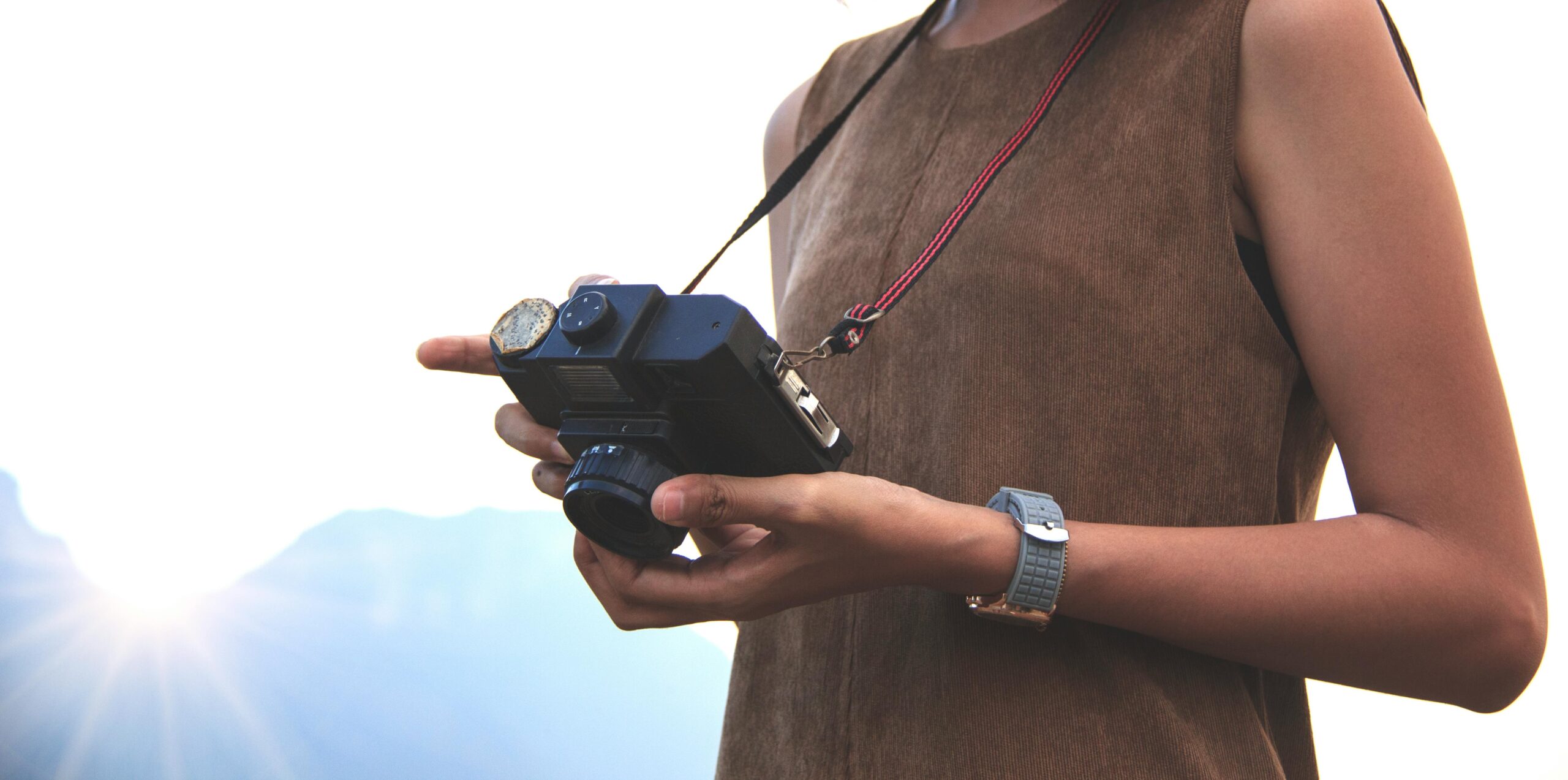 A close-up of a woman holding a vintage camera outdoors during sunrise, capturing the beauty of nature.